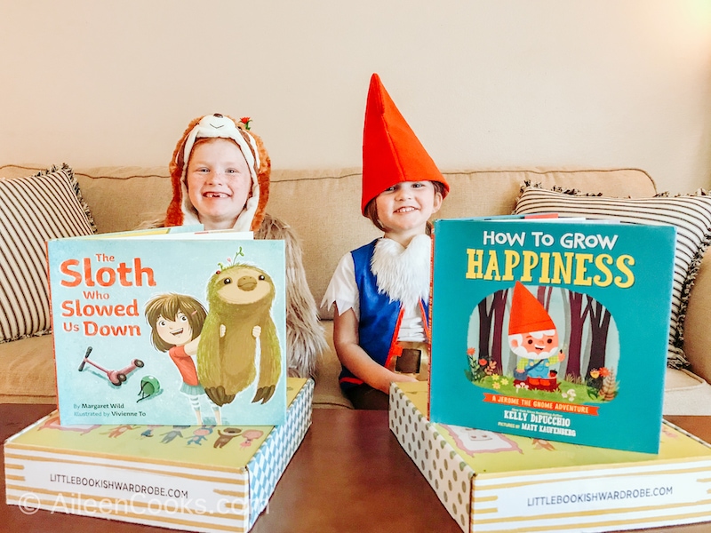 Two kids sitting on a couch in costumes next to two children's books.