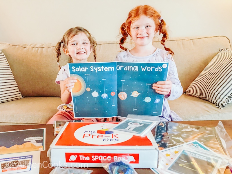 Two girls smiling and holding up a map of the solar system.