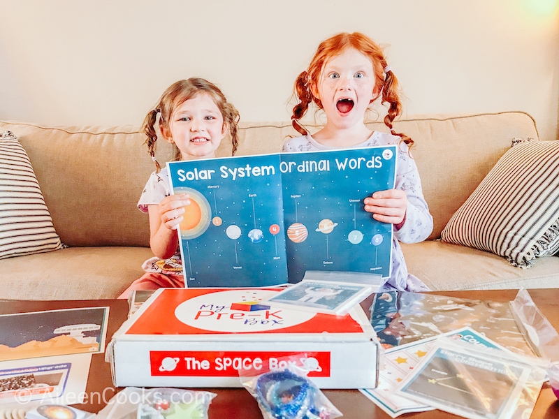 Two girls excited and holding up a map of the solar system.