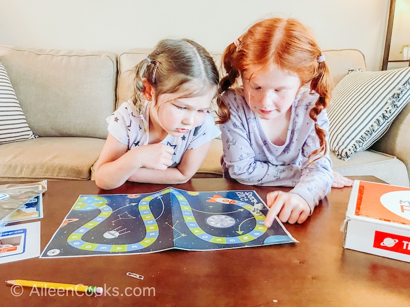 Two little girls leaning over a space-themed board game.