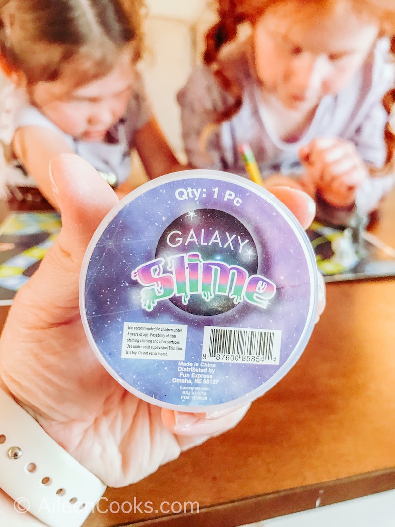 A hand holding up a round jar of slime.