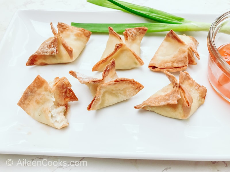 A white platter of six crab rangoon, with one bitten out of.