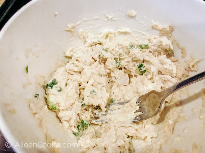 Crab meat, cream cheese, green onions, and spices mixed up inside a white bowl.