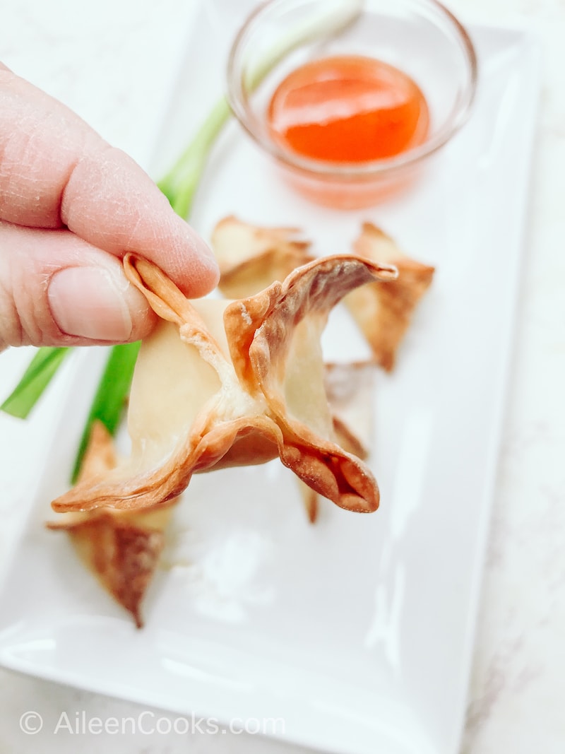 A hand holding up a fried crab rangoon.