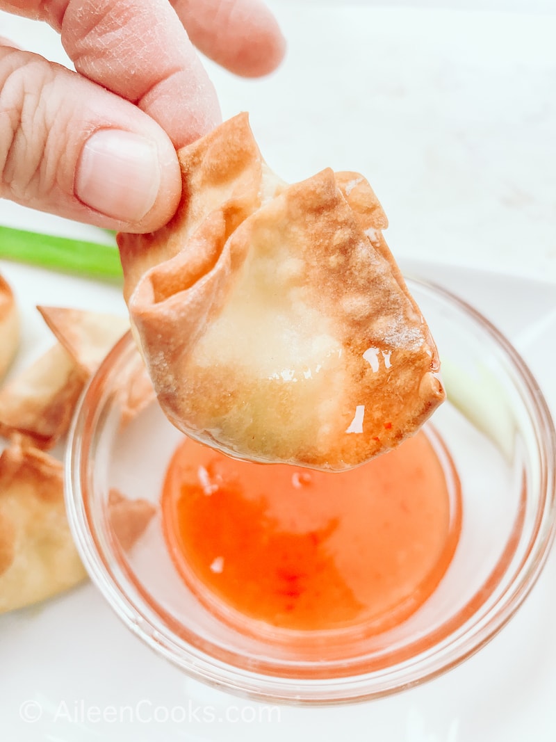 A crab rangoon being dipped into orange sauce.