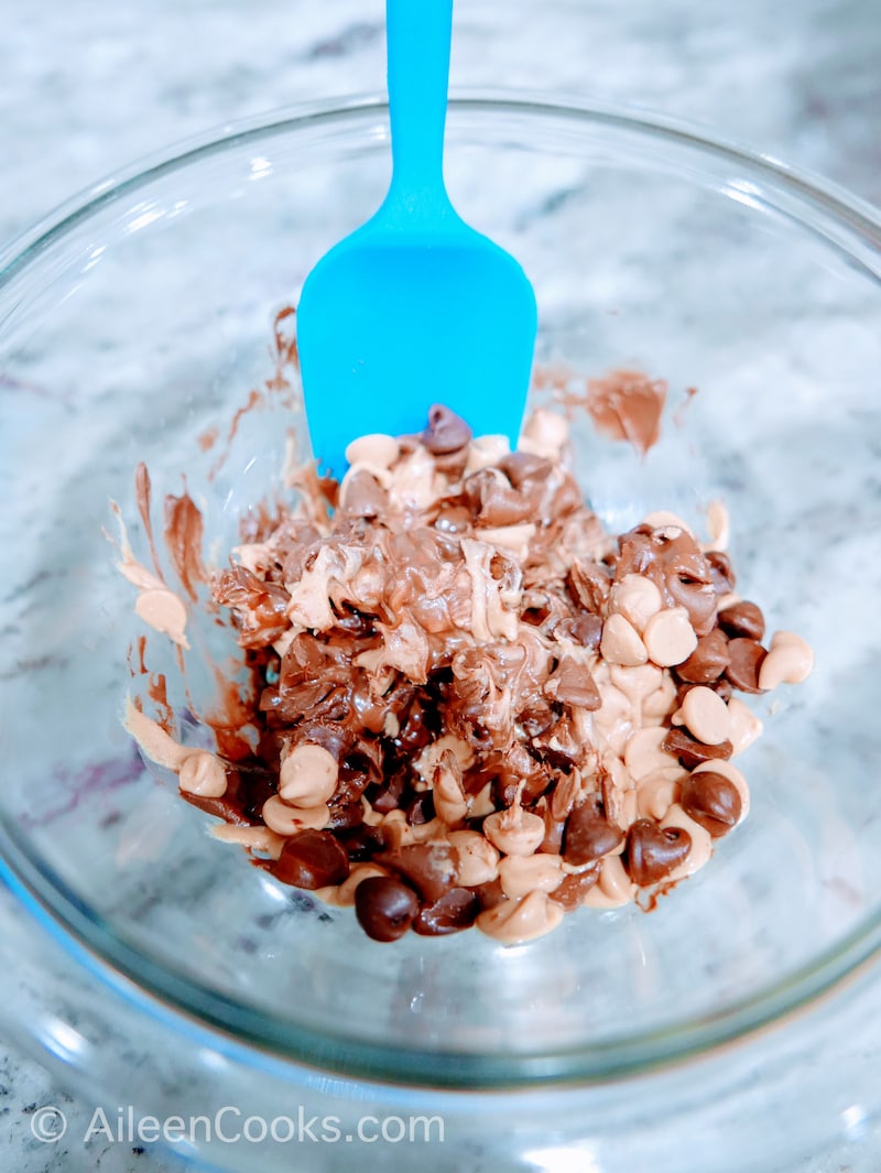 Chocolate and peanut butter chips in a glass bowl with a blue spoon.