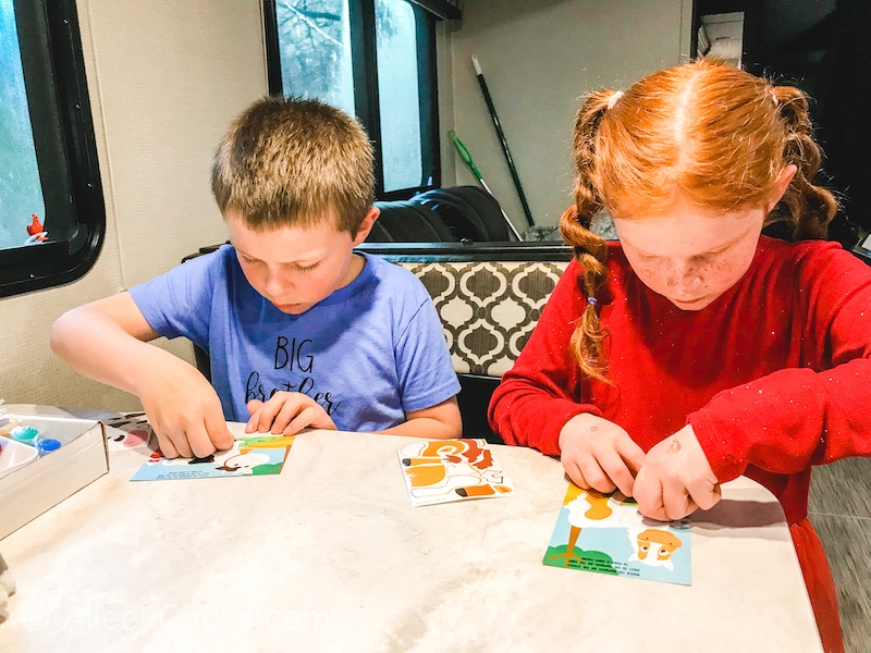 Two kids working on a sticker project at a white table.