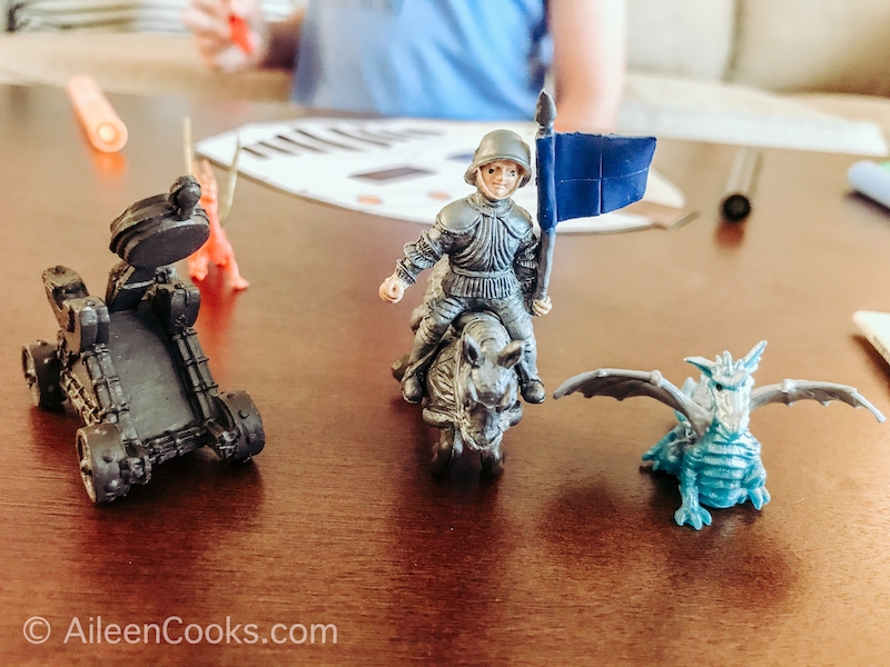 Three small toy figurines on a table, including a knight, dragon, and horse.