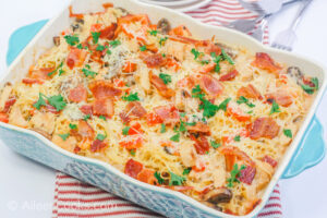 A blue casserole dish filed with a casserole made of chicken, pasta, and bacon.