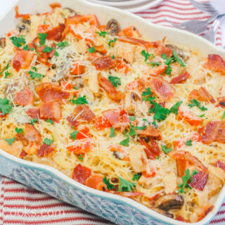 A blue casserole dish filed with a casserole made of chicken, pasta, and bacon.