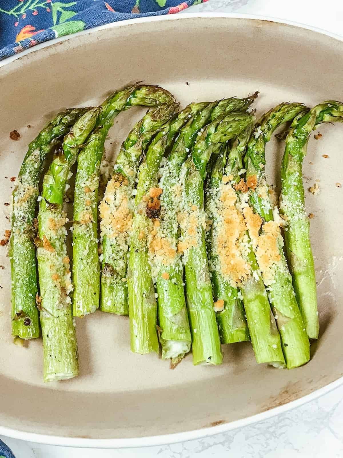 An oval baking dish filled with roasted asparagus topped with golden brown parmesan cheese.