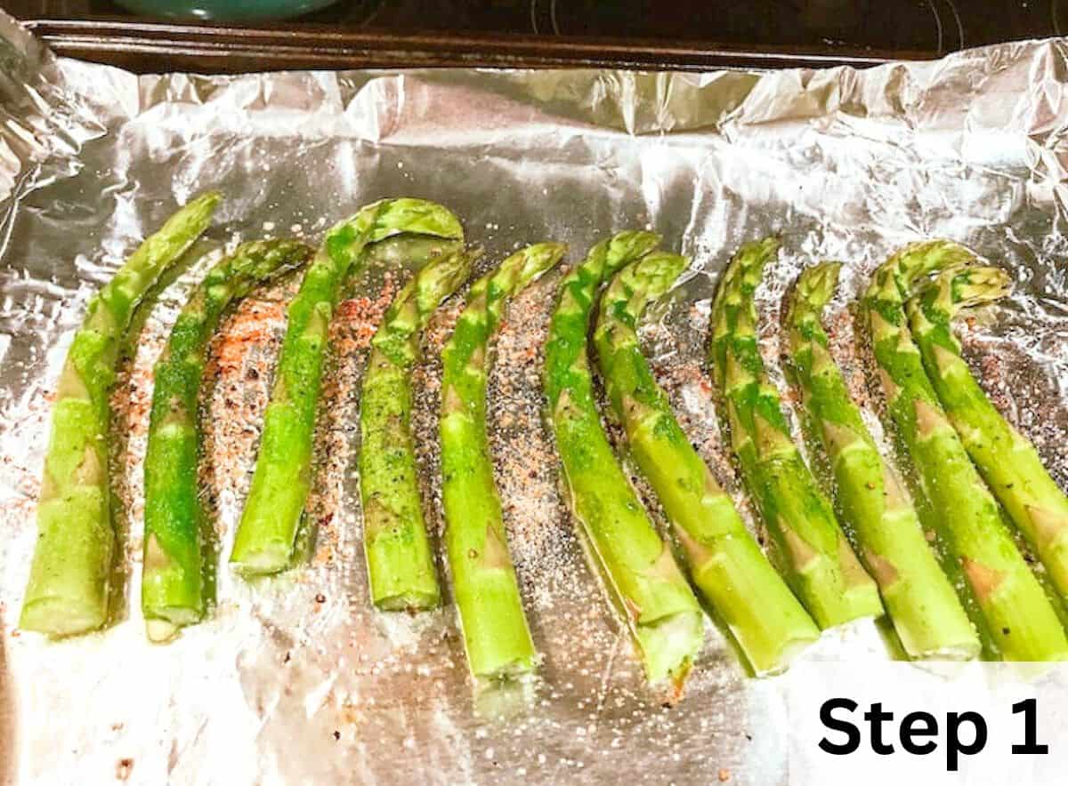 Fresh asparagus lined up on a foiled lined baking sheet and coated in seasonings. 