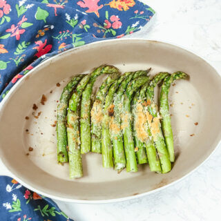 Roasted asparagus topped with parmesan in an oval serving dish.