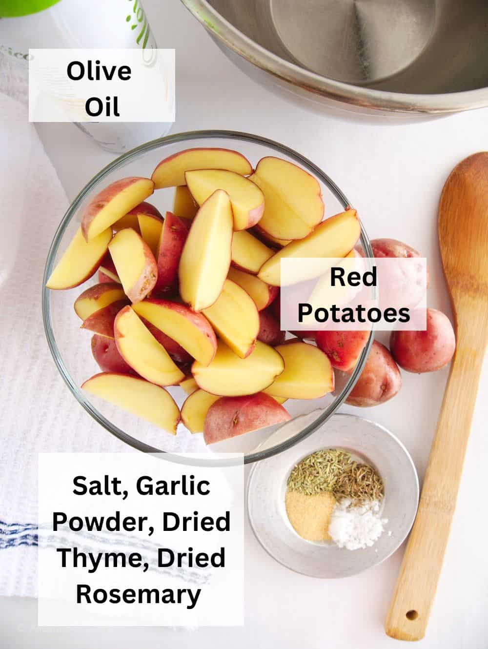 A clear glass bowl of quartered red potatoes next to a smaller glass bowl of spices.