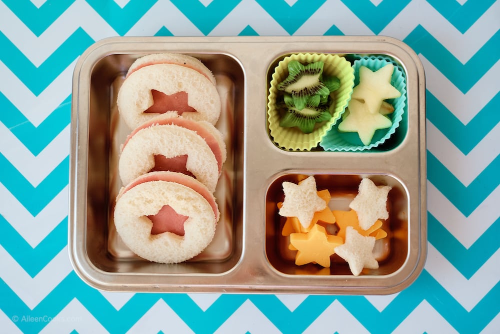 A silver bento box filled with sandwiches, fruit, and cheese; all cut into star shapes.