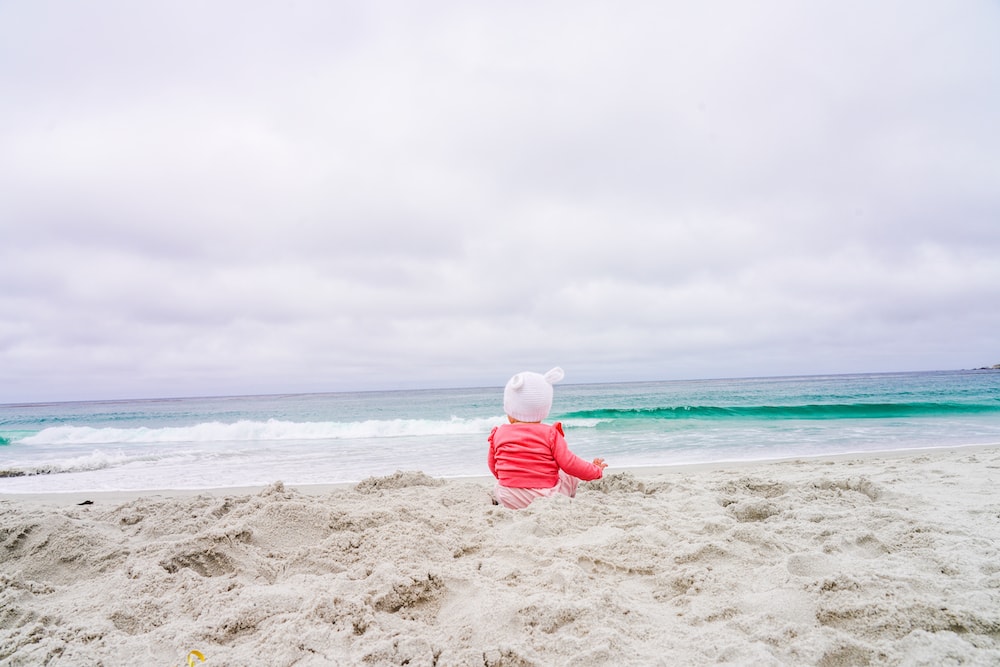 A baby sitting on Carmel Beach, looking at the Pacific Ocean.