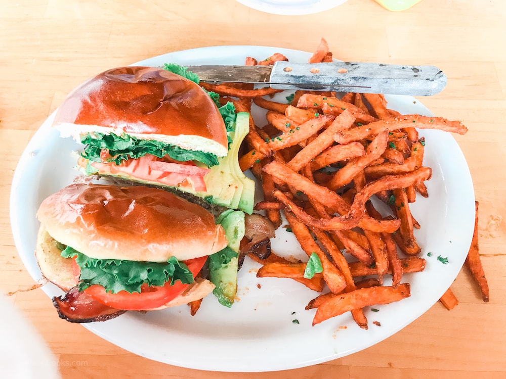 A cheeseburger cut in half, next to a large pile of sweet potato fries.