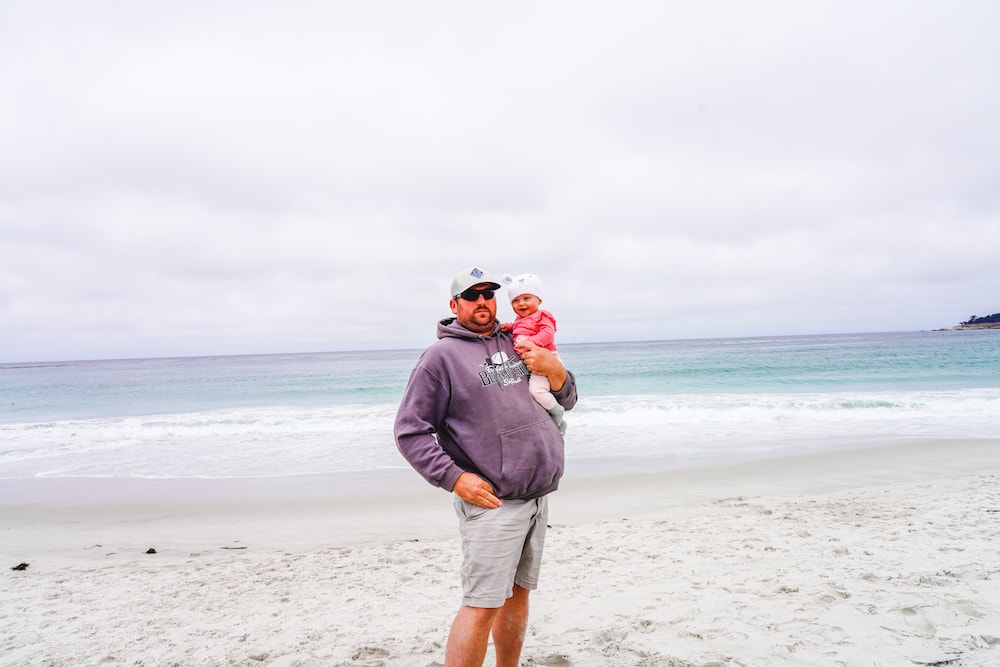 A father and baby daughter standing in front of the Pacific Ocean at Carmel Beach.