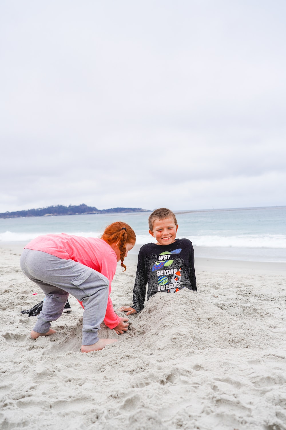 A girl burying a boy. in the sand at Carmel Beach