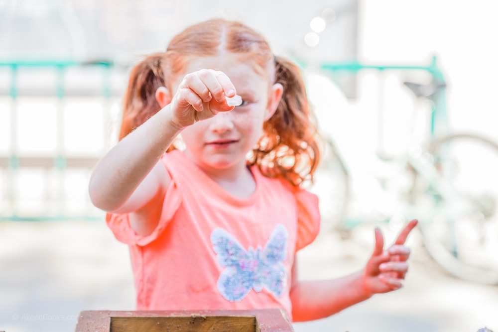 A little girl with red hair, holding up a gem she found during gem mining at Jellystone Park.