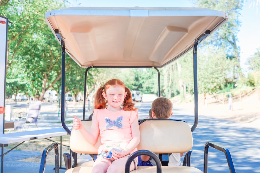 A girl sitting on the back of a go cart, giving a thumbs up.