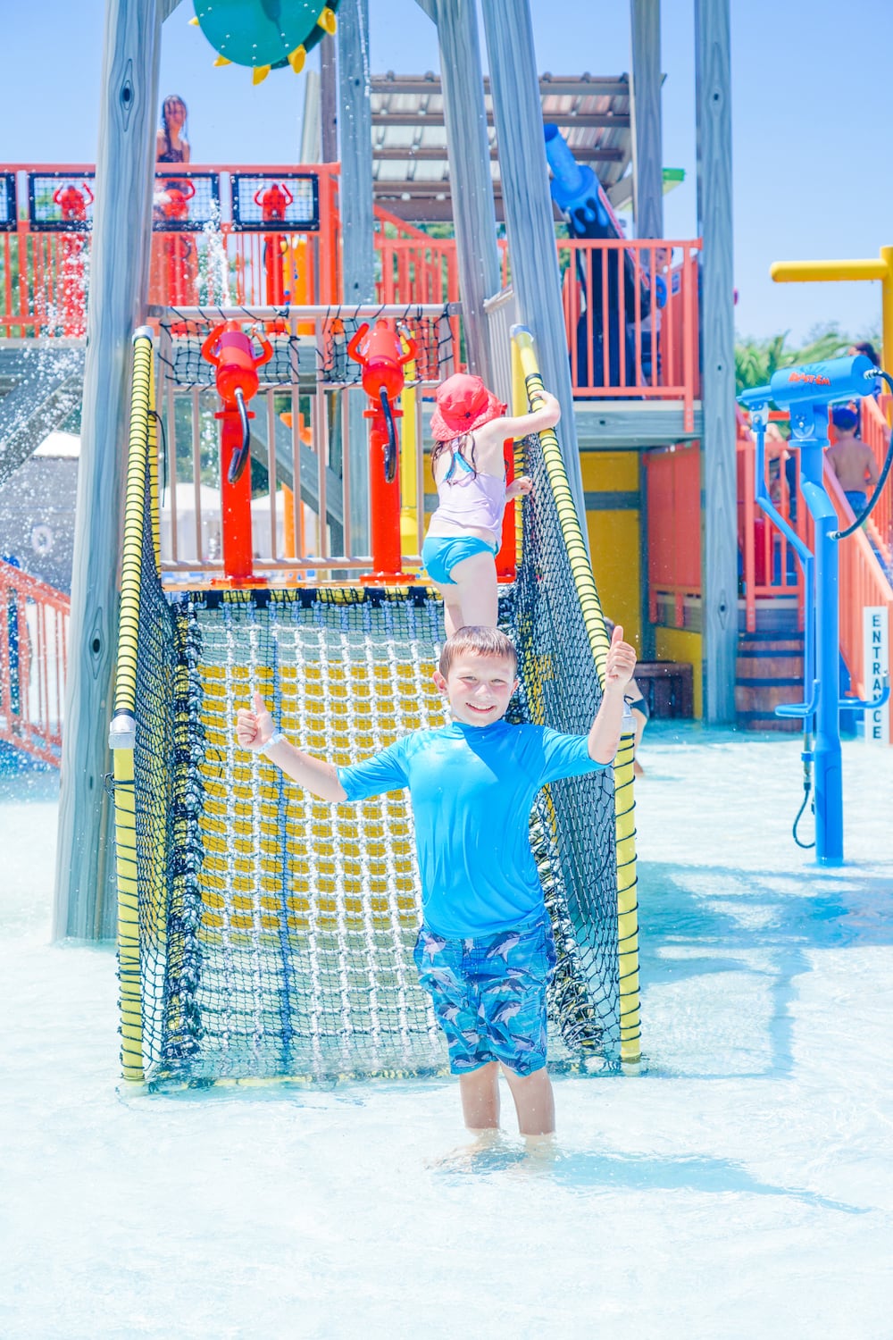 A boy in a blue swim suit standing inside the Jellystone Park water playground.