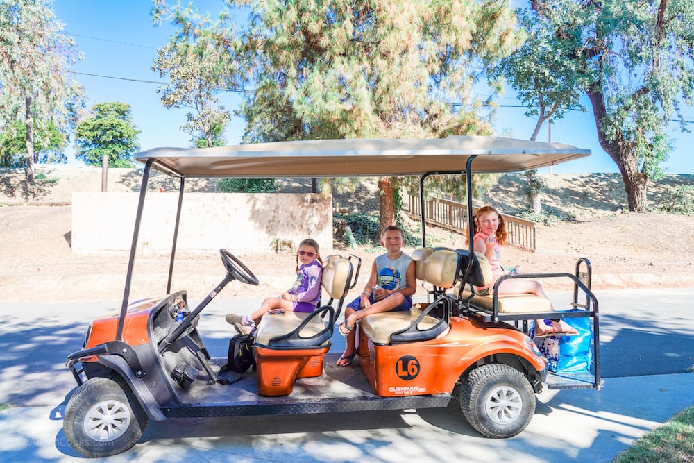 Three kids sitting inside of a large golf cart.