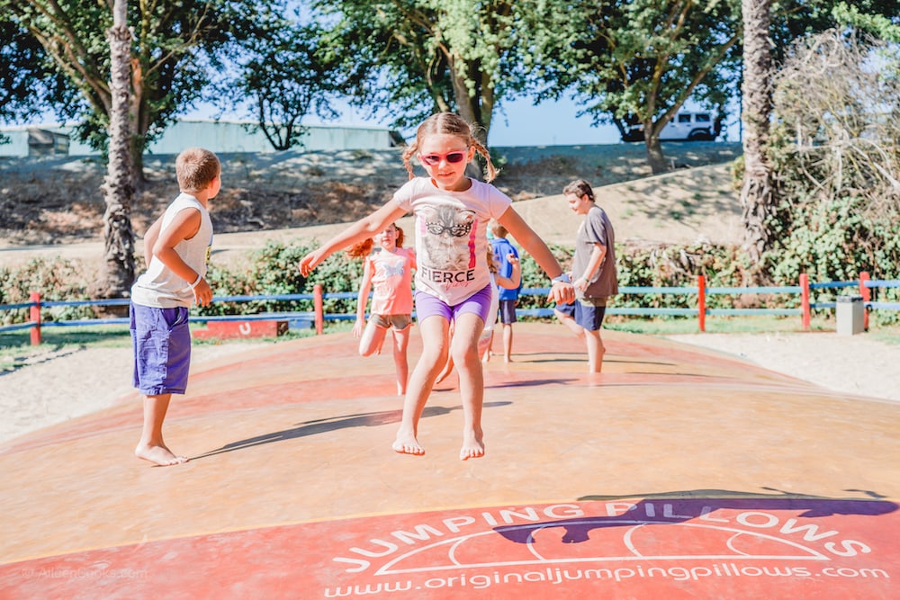 A little girl with brown hair, jumping on a jumping pillow.