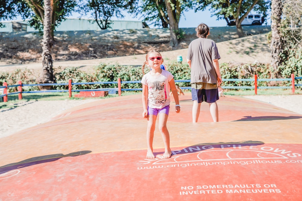 A brown-haired girl standing on a jumping pillow.