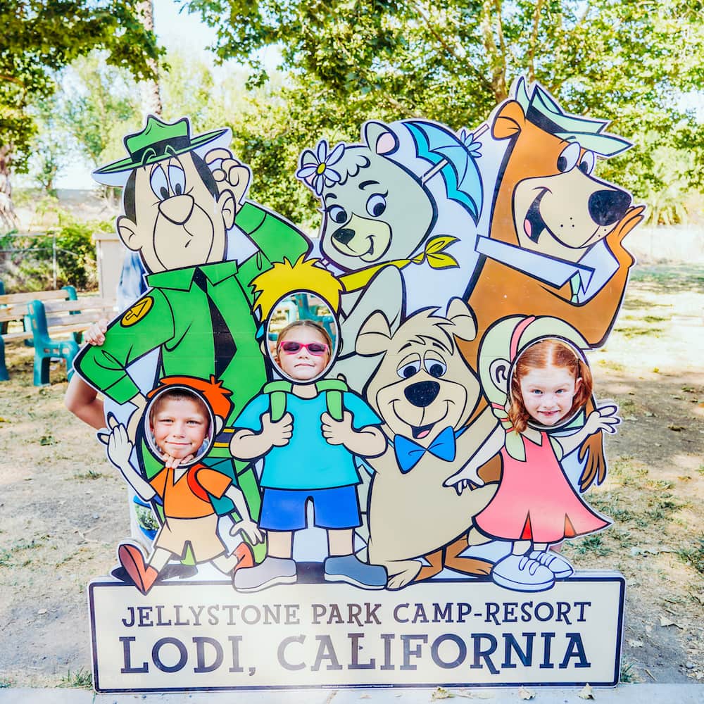 Three kids with their faces in the holes of a Jellystone Park photo opp.