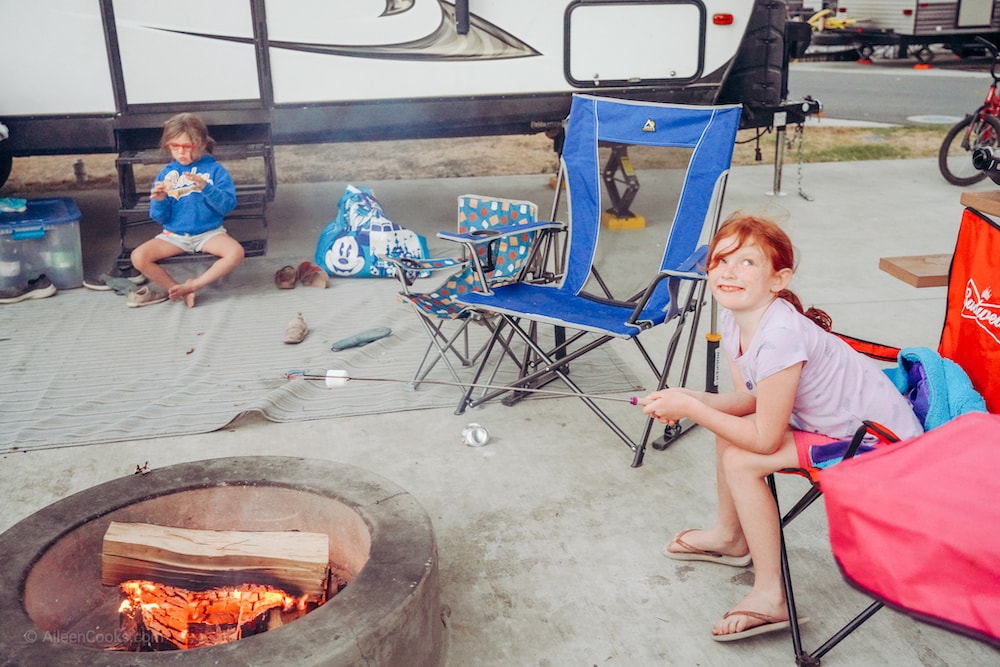 A girl sitting in front of a campfire and smiling.