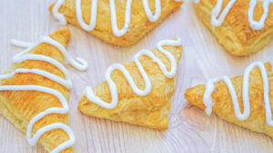 Pumpkin hand pies drizzled with white icing, on top of parchment paper.
