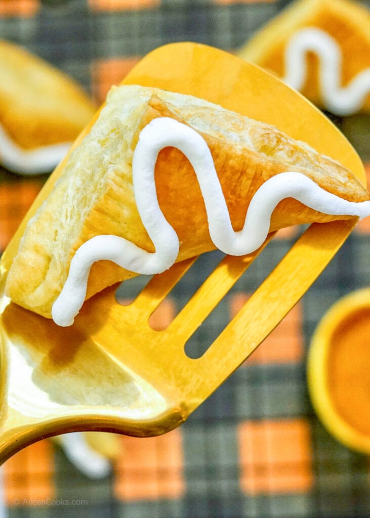 A pumpkin hand pie on a gold spatula.