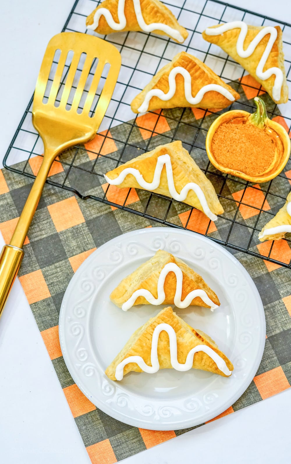 Two pumpkin hand pies on a white plate, next to a cooling rack of pumpkin hand pies.