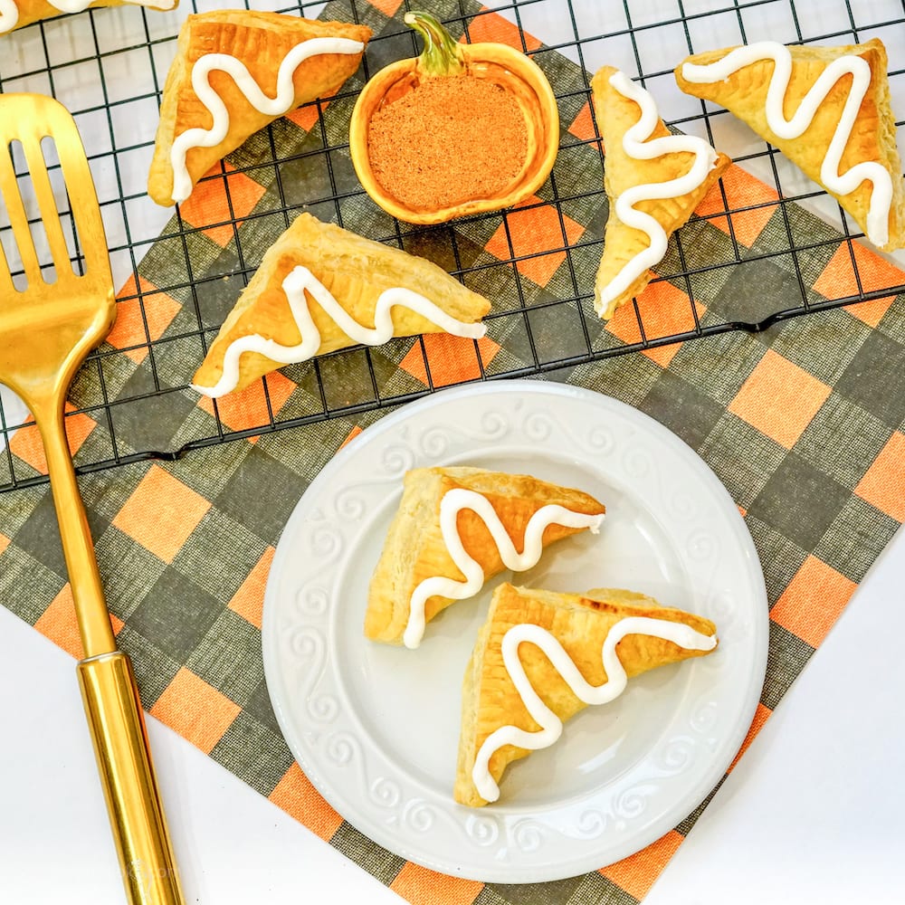 An orange and black checkered placemat topped with a cooling rack of pumpkin hand pies.