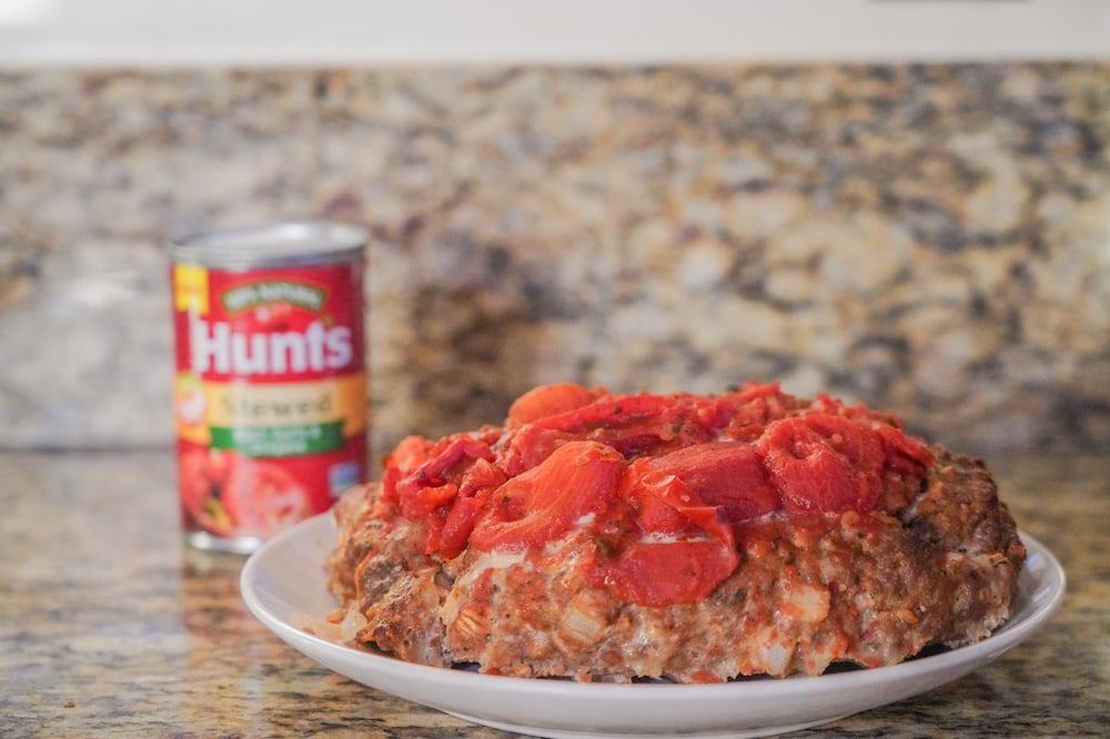 A dish of meatloaf, topped with stewed tomatoes.