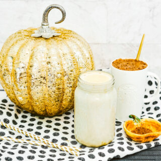 A jar of homemade creamer in front of a white mug of coffee and decorative pumpkin.