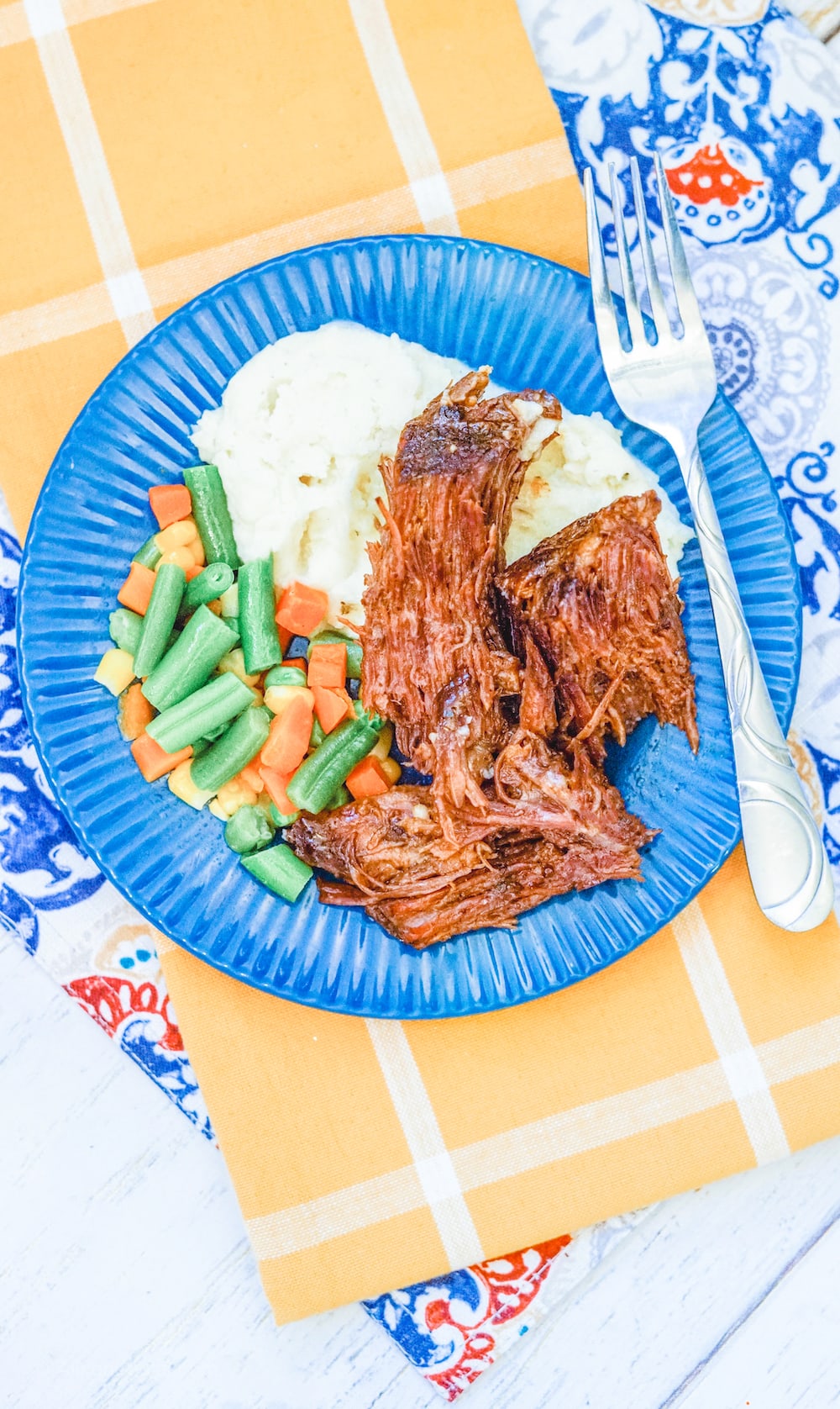 A yellow cloth napkin under a blue plate of Mississippi pot roast.