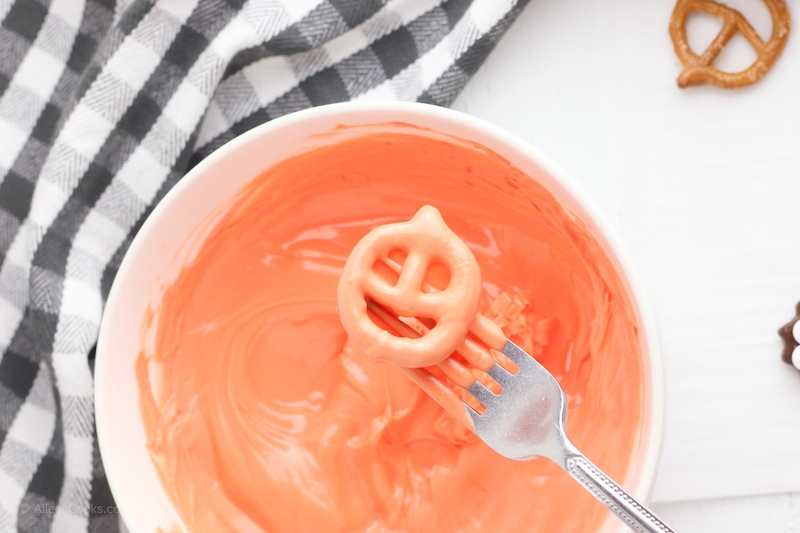 A pumpkin shaped pretzel dipped in orange melted candy.