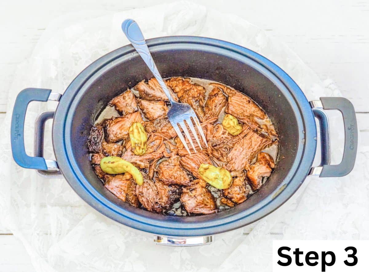 A fork sticking out of a slow cooker full of cooked pot roast and peperoncinis.