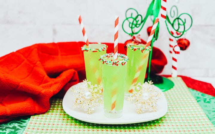 A festive table decorated for Christmas with three green shots topped with red and white straws.