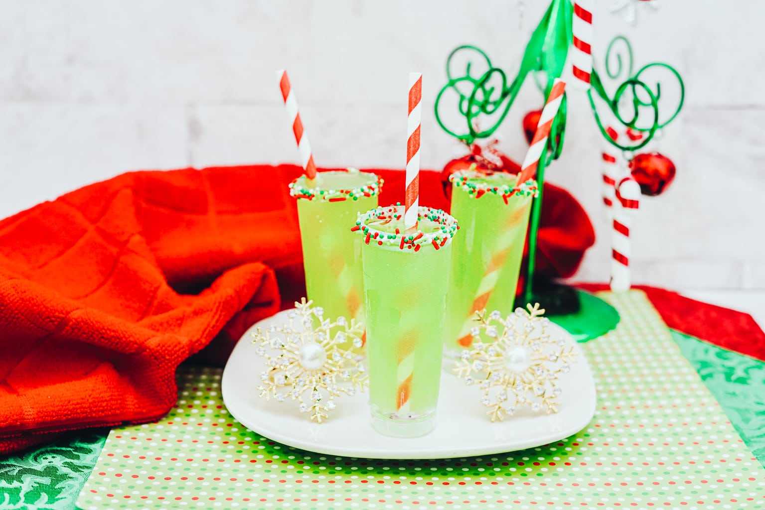 A festive table decorated for Christmas with three green shots topped with red and white straws.