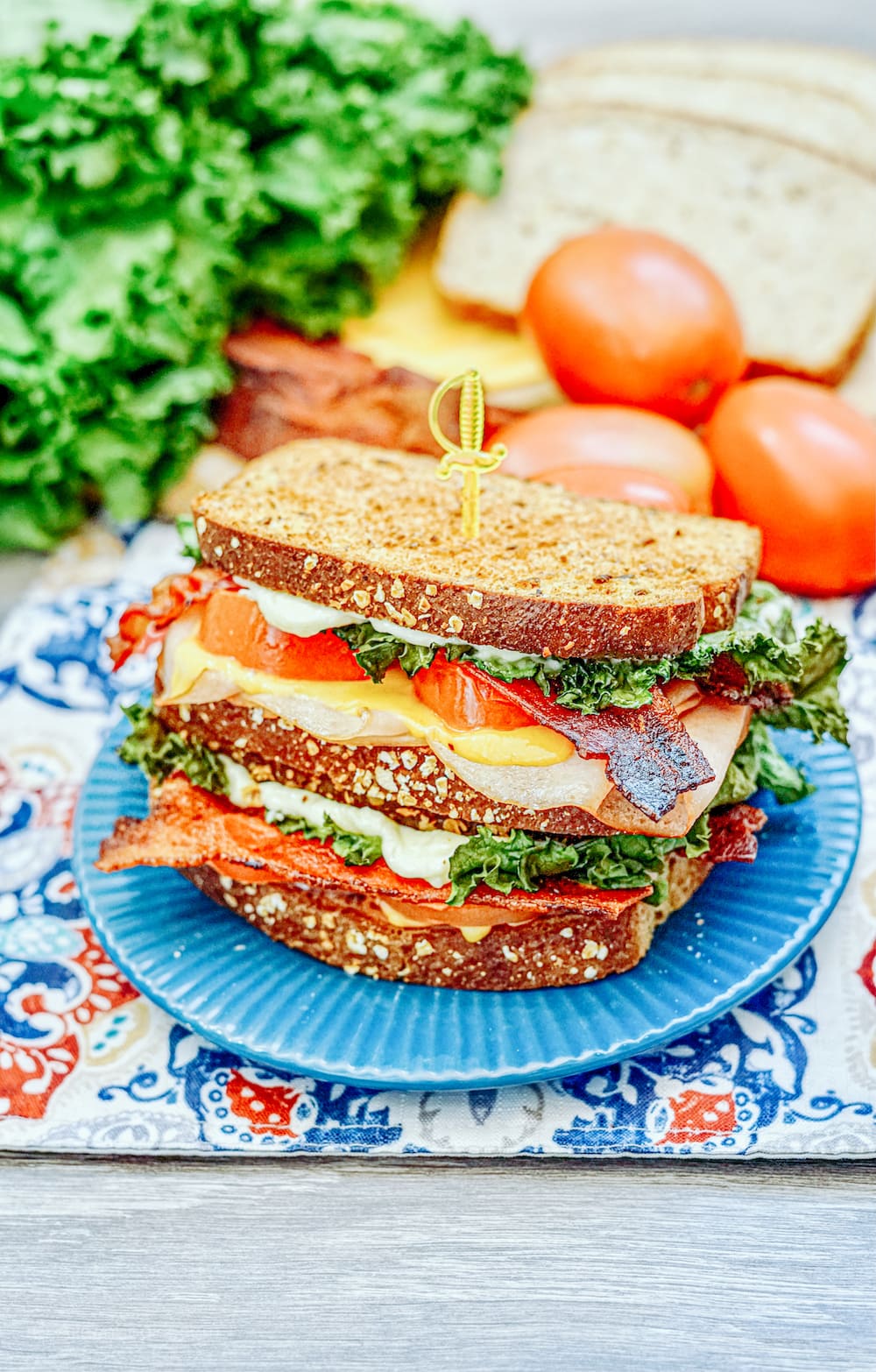 A blue plate loaded with an air fryer turkey club sandwich next to a stack of lettuce and tomatoes. 