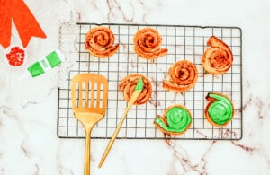 Cinnamon rolls on a cooling rack, being frosted with green frosting.