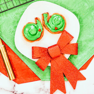 A white plate with two grinch cinnamon rolls and a red decorative bow.