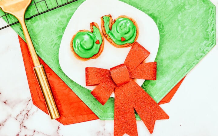 A white plate with two grinch cinnamon rolls and a red decorative bow.