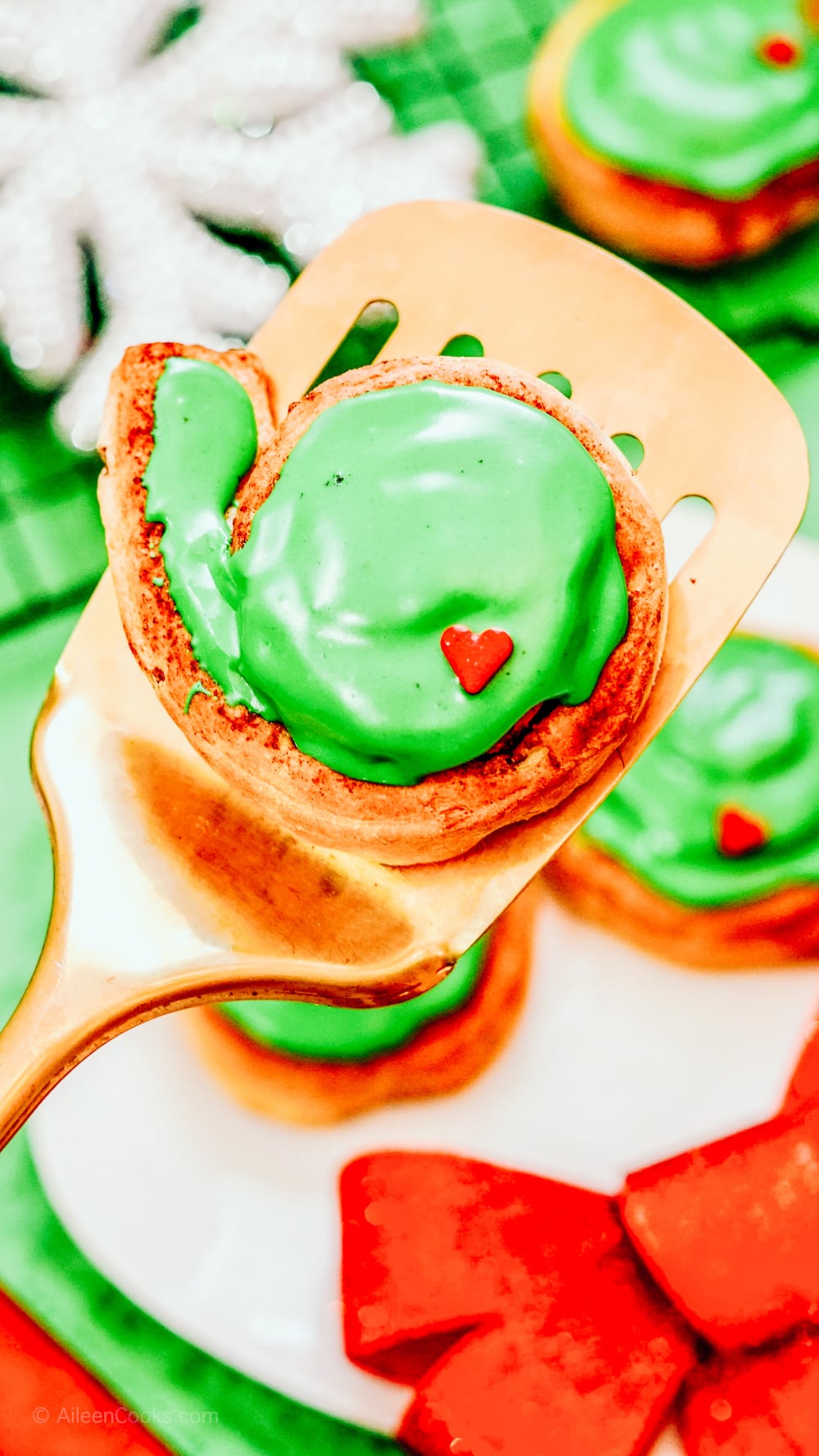 A gold spatula holding up a Grinch Cinnamon Roll.