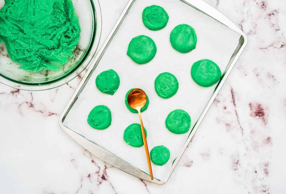 Green cookie dough balls on a parchment-lined cookie sheet.