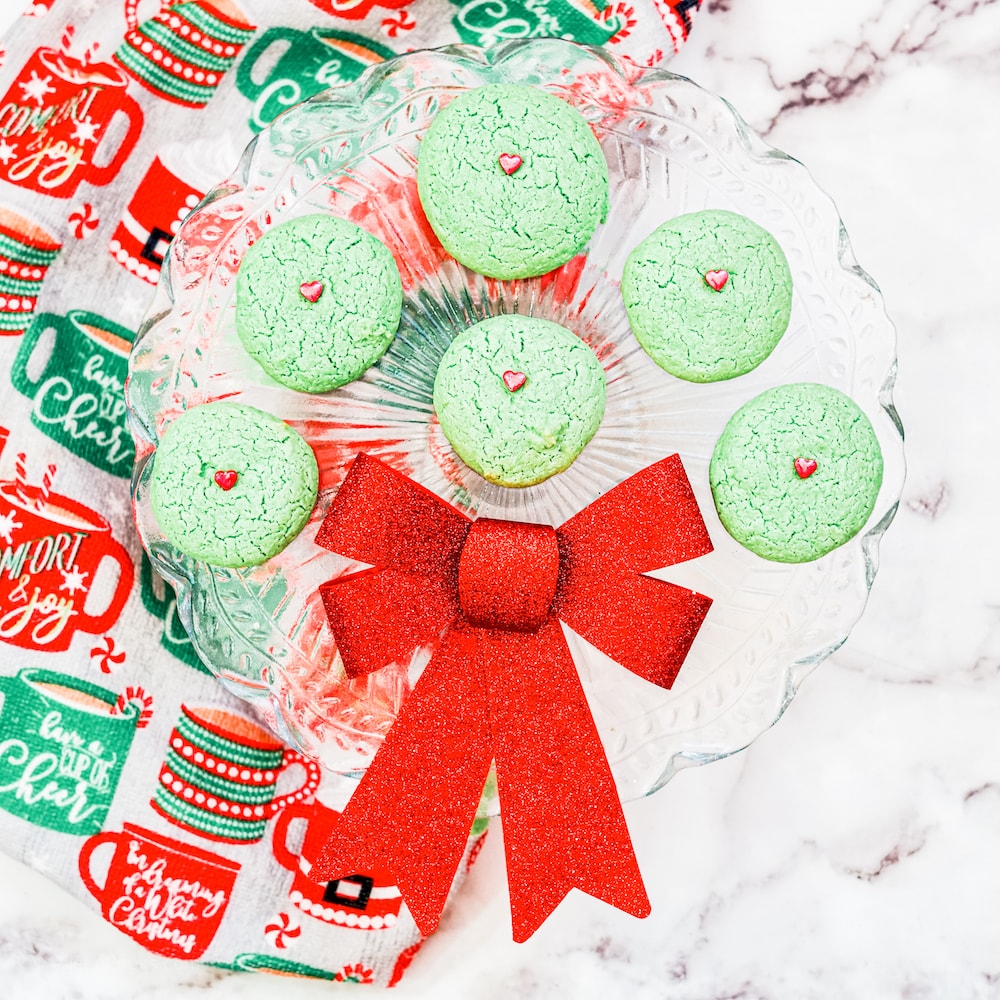 A clear tray holding seven grinch cookies with a red bow in the middle. 