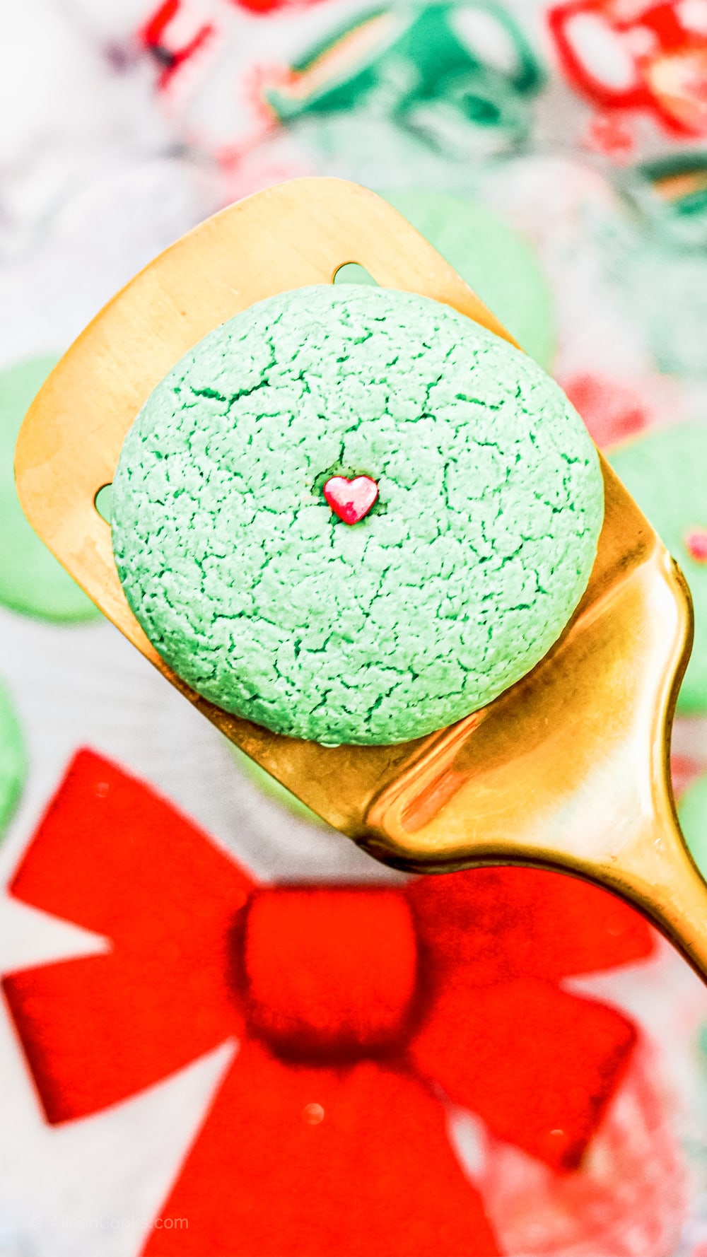 A gold spatula holding up a green grinch sugar cookie.
